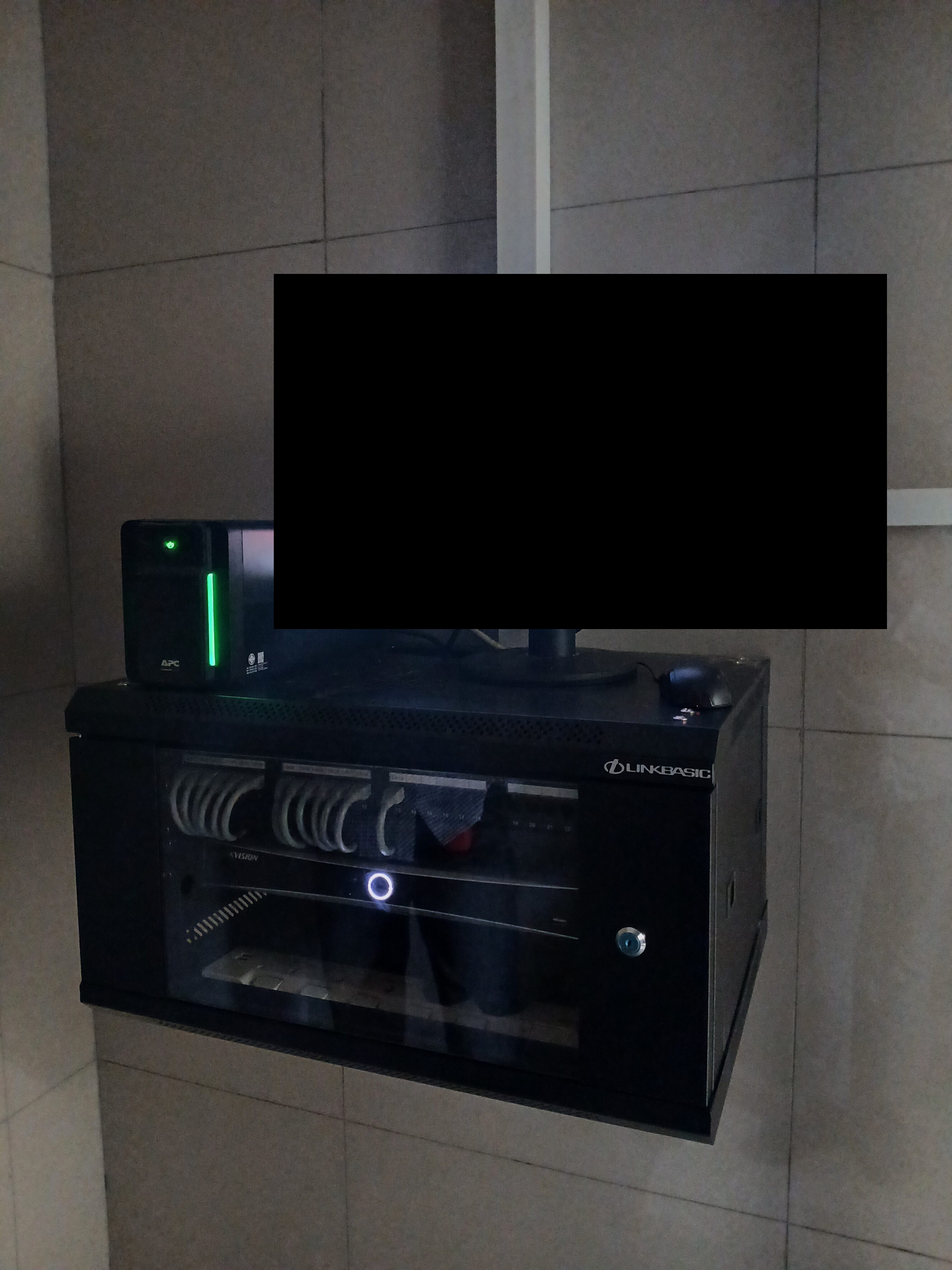 NVR and UPS installed in wall-mounted cabinet, monitor display blacked out for privacy